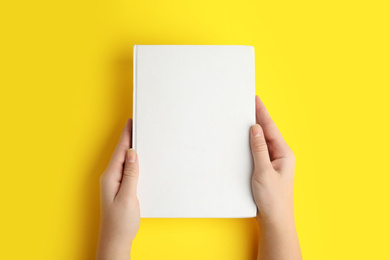 Photo of Woman holding book with blank cover on yellow background, top view