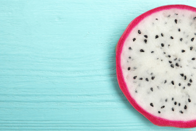 Photo of Slice of delicious dragon fruit (pitahaya) on light blue wooden table, top view. Space for text