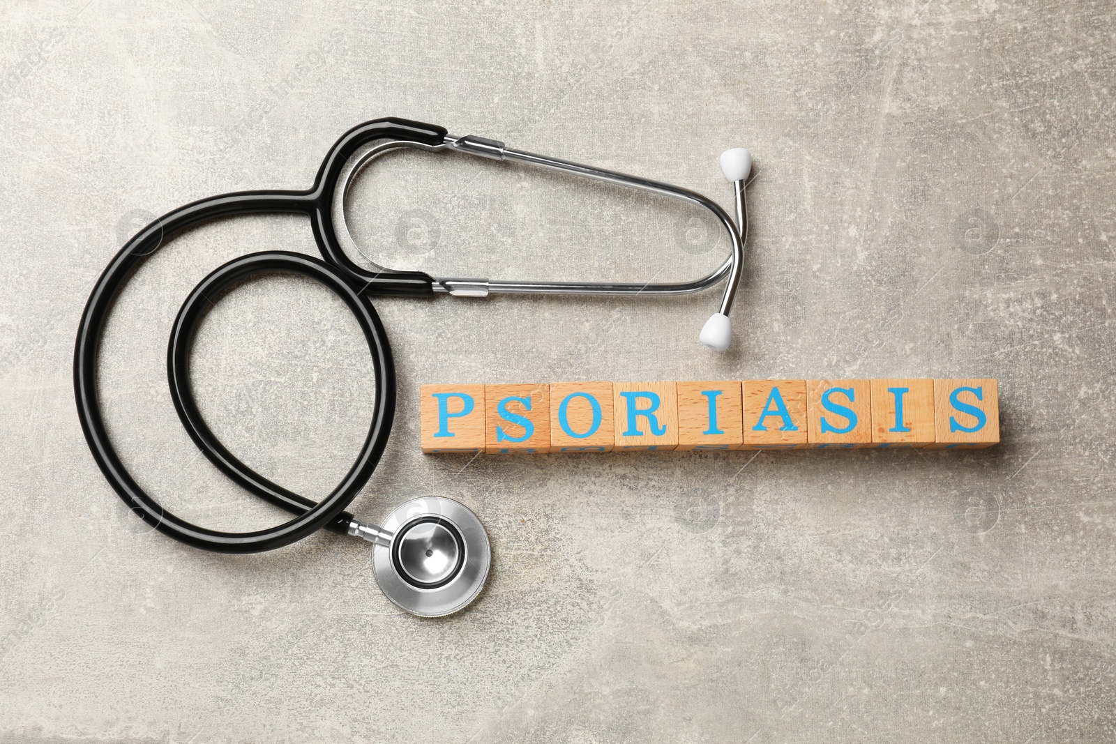 Photo of Word Psoriasis made of wooden cubes with letters and stethoscope on light gray textured table, flat lay