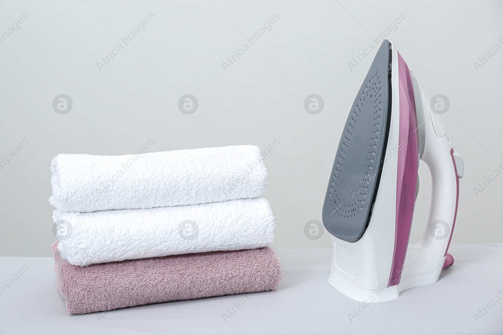 Photo of Modern iron and clean towels on table against light grey background