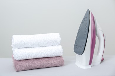 Modern iron and clean towels on table against light grey background