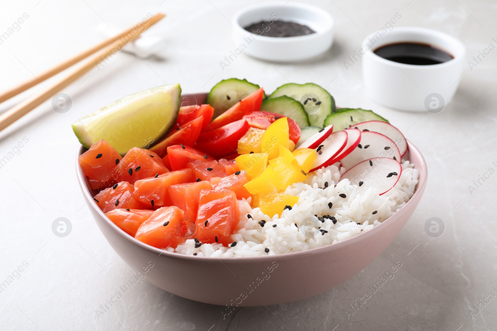 Photo of Delicious poke bowl with salmon, rice and vegetables served on light grey table