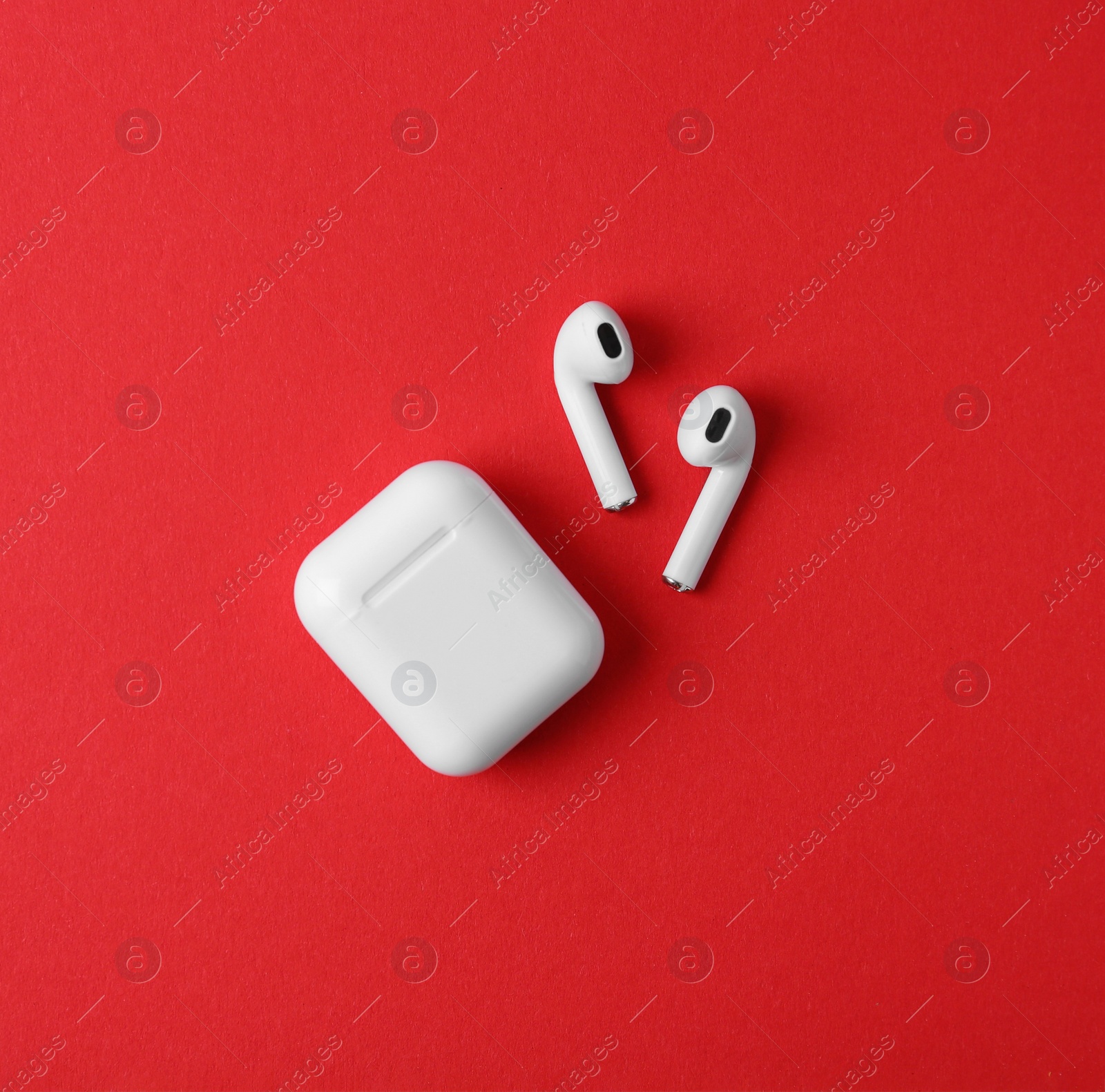 Photo of Modern wireless earphones and charging case on red background, flat lay