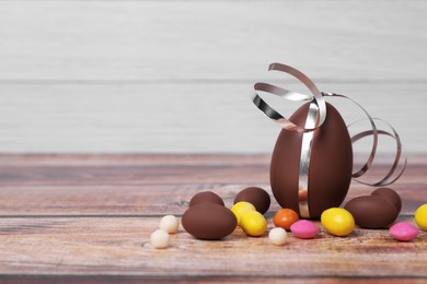 Photo of Delicious chocolate eggs and colorful candies on wooden table. Space for text