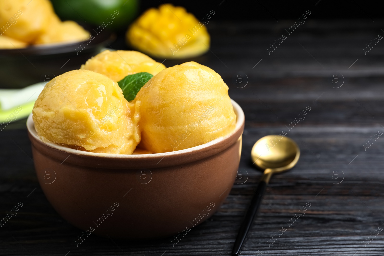 Photo of Yummy mango ice cream in bowl on black wooden table. Space for text