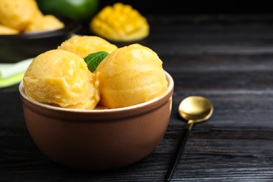 Photo of Yummy mango ice cream in bowl on black wooden table. Space for text