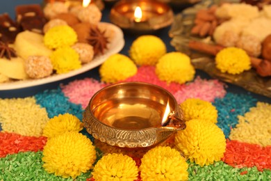 Diwali celebration. Tasty Indian sweets, colorful rangoli and diya lamps on table, closeup