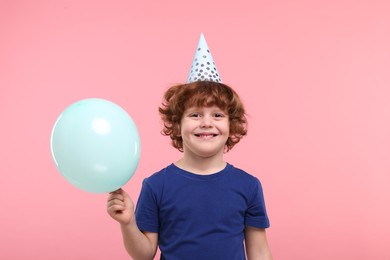 Happy little boy in party hat with balloon on pink background