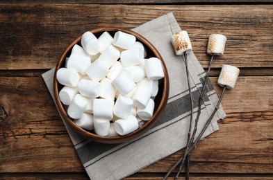 Photo of Sticks with roasted marshmallows on wooden table, flat lay