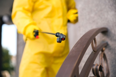 Photo of Person in hazmat suit disinfecting railing, focus on sprayer. Surface treatment during coronavirus pandemic