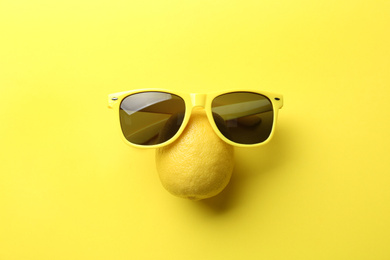 Photo of Juicy lemon and sunglasses on yellow background, top view