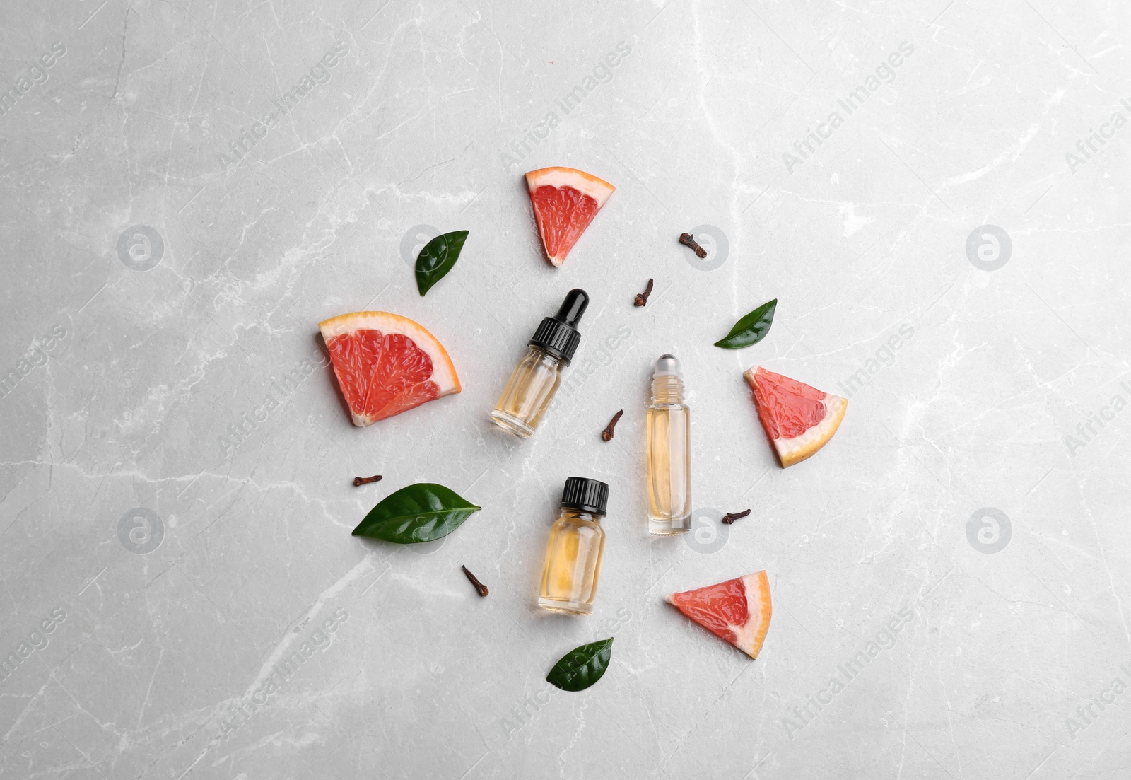 Photo of Flat lay composition with grapefruit slices and bottles of essential oil on grey background