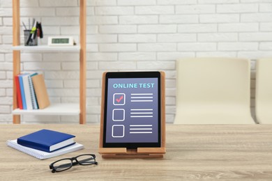 Photo of Modern tablet with online test, notebooks and glasses  on table in office