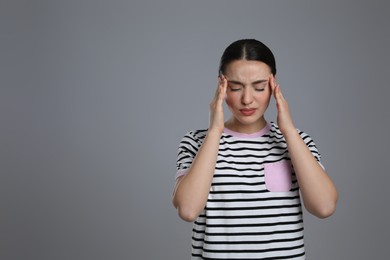 Photo of Young woman suffering from headache on grey background, space for text. Cold symptoms