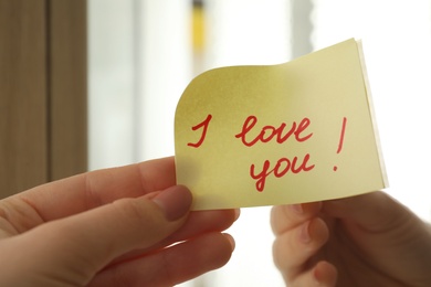 Photo of Woman putting sticky note with text I love you! on mirror, closeup