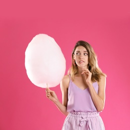 Photo of Emotional young woman with cotton candy on pink background