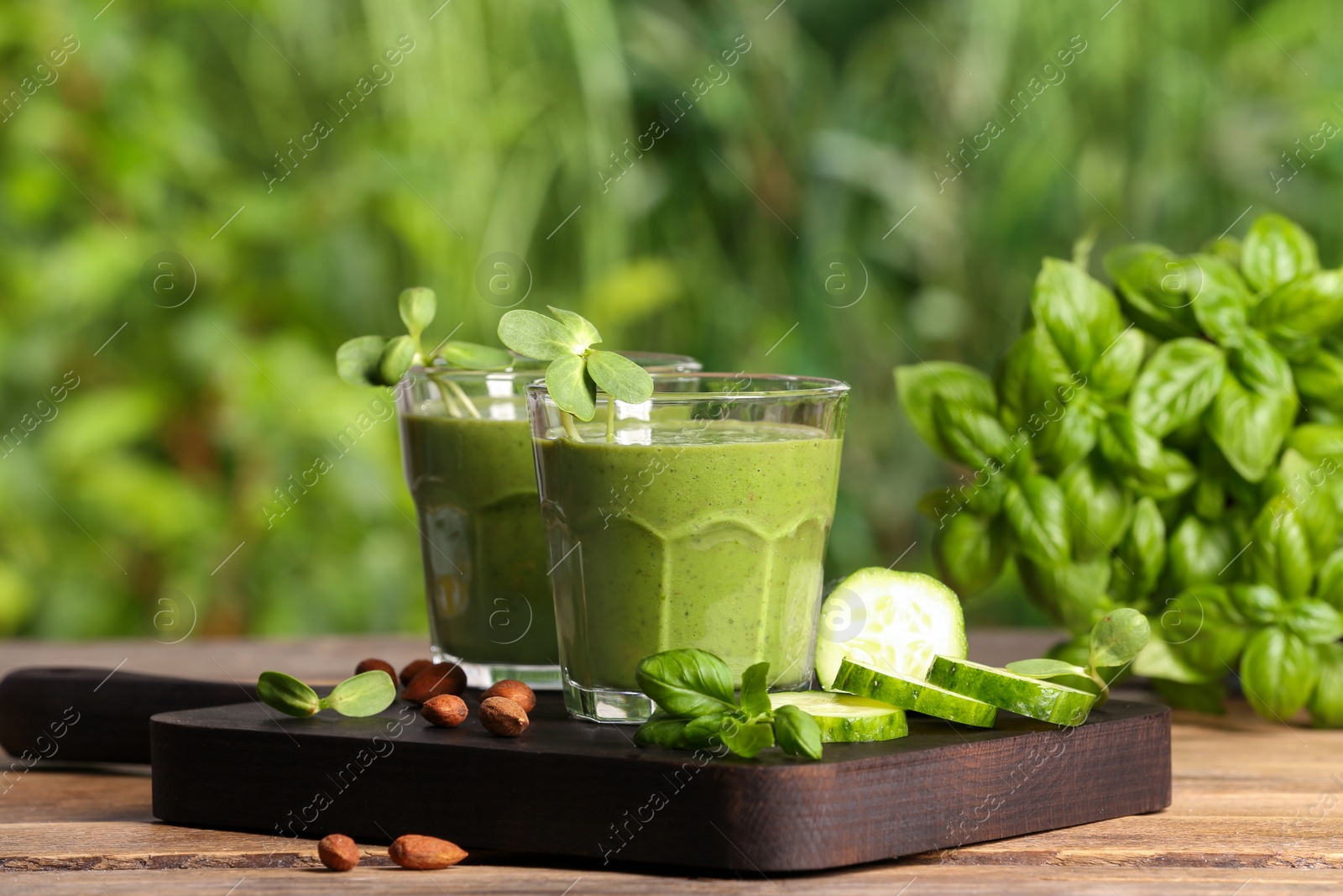 Photo of Glasses of fresh green smoothie and ingredients on wooden table outdoors