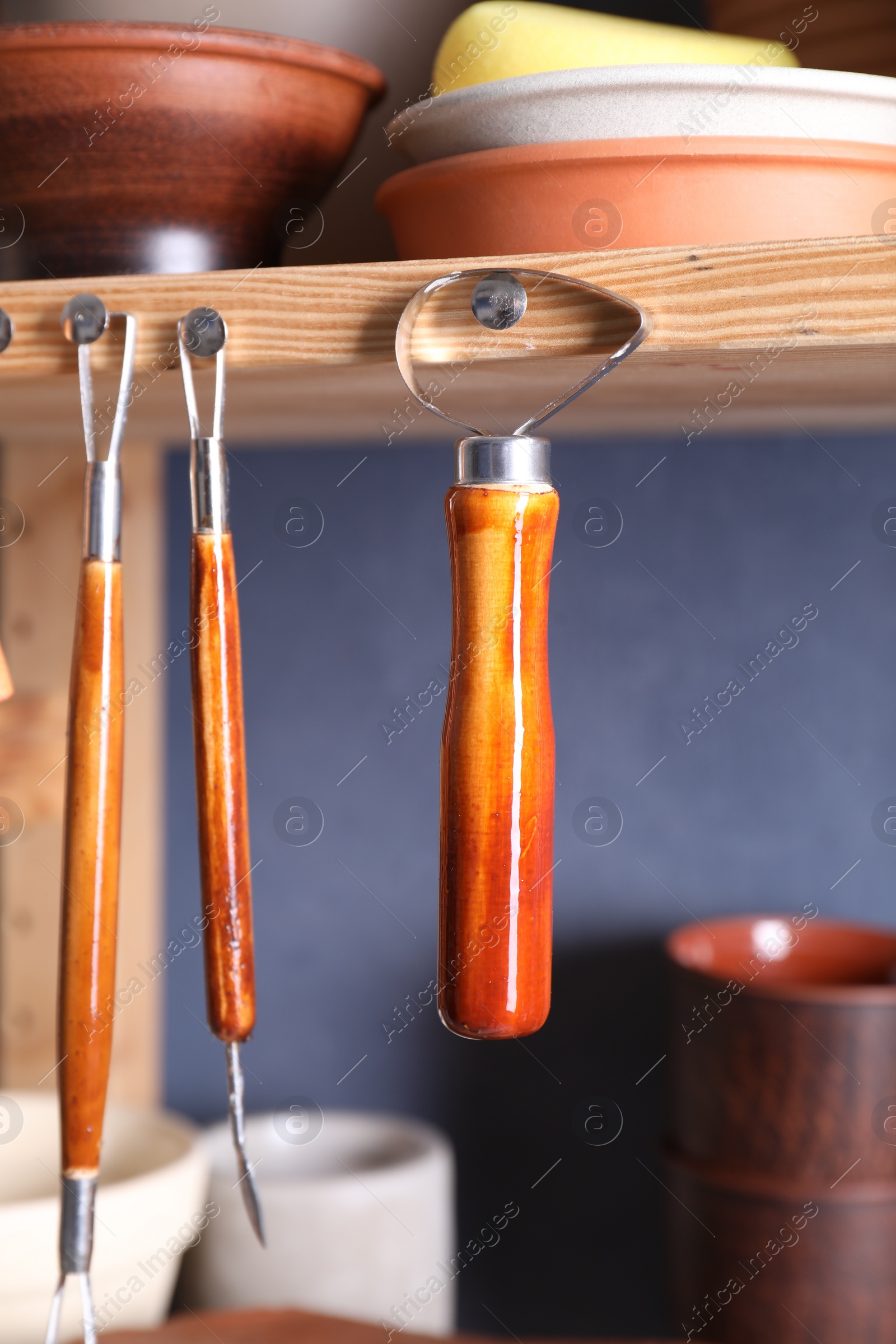 Photo of Set of different crafting tools and clay dishes on wooden rack in workshop, closeup