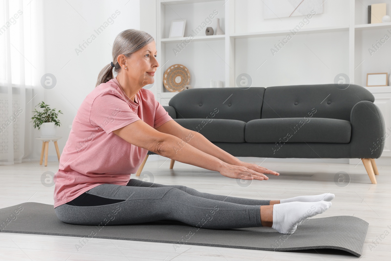 Photo of Senior woman in sportswear stretching on fitness mat at home