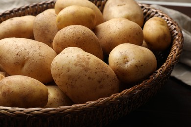 Raw fresh potatoes in wicker basket on wooden table, closeup