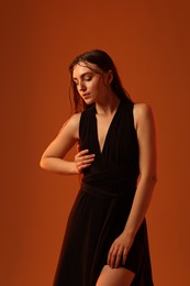 Beautiful woman in black dress posing on brown background