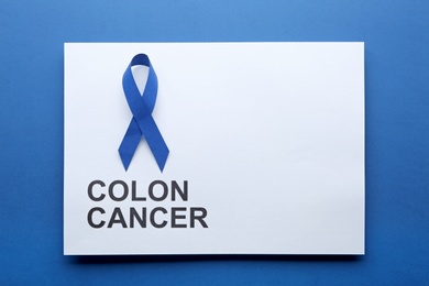 Photo of Card with words COLON CANCER and blue awareness ribbon on color background, top view. Space for text