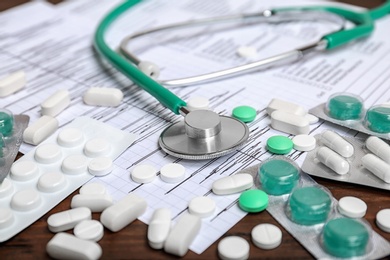 Stethoscope, forms and pills on wooden background. Cardiology service