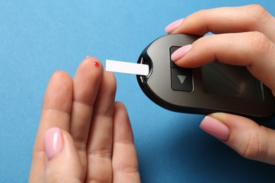 Diabetes. Woman checking blood sugar level with glucometer on light blue background, closeup