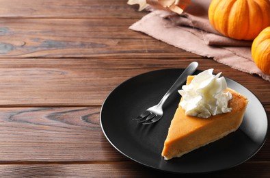 Photo of Piece of delicious pumpkin pie with whipped cream and fork on wooden table, space for text