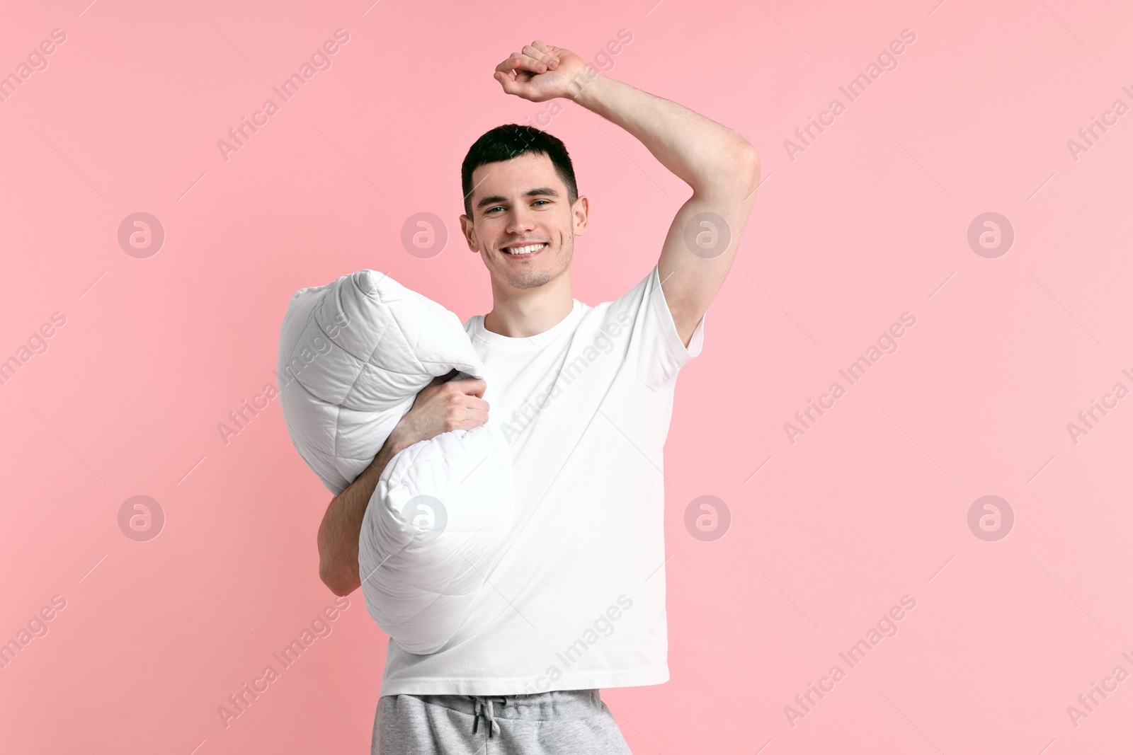 Photo of Happy man in pyjama holding pillow on pink background