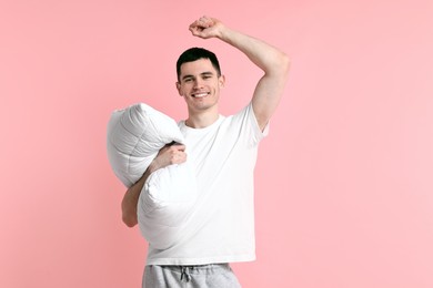 Happy man in pyjama holding pillow on pink background