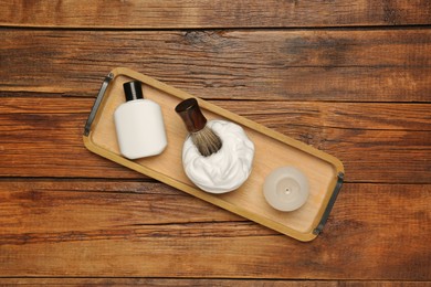 Photo of Tray with shaving brush, foam, lotion and candle on wooden table, top view