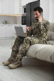 Photo of Soldier with laptop talking on phone at home. Military service