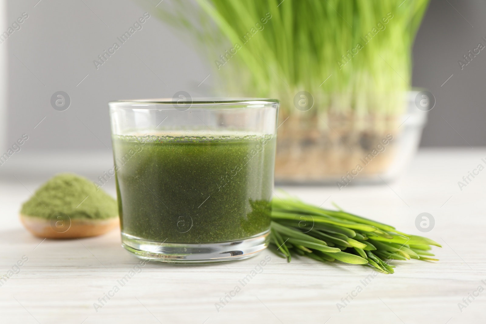 Photo of Wheat grass drink in glass and fresh sprouts on white wooden table, closeup