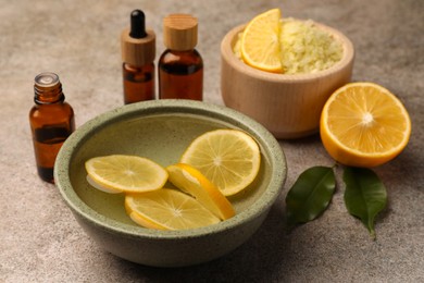 Photo of Essential oil with lemons and sea salt on grey textured table. Aromatherapy treatment