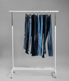 Photo of Rack with different jeans on grey background