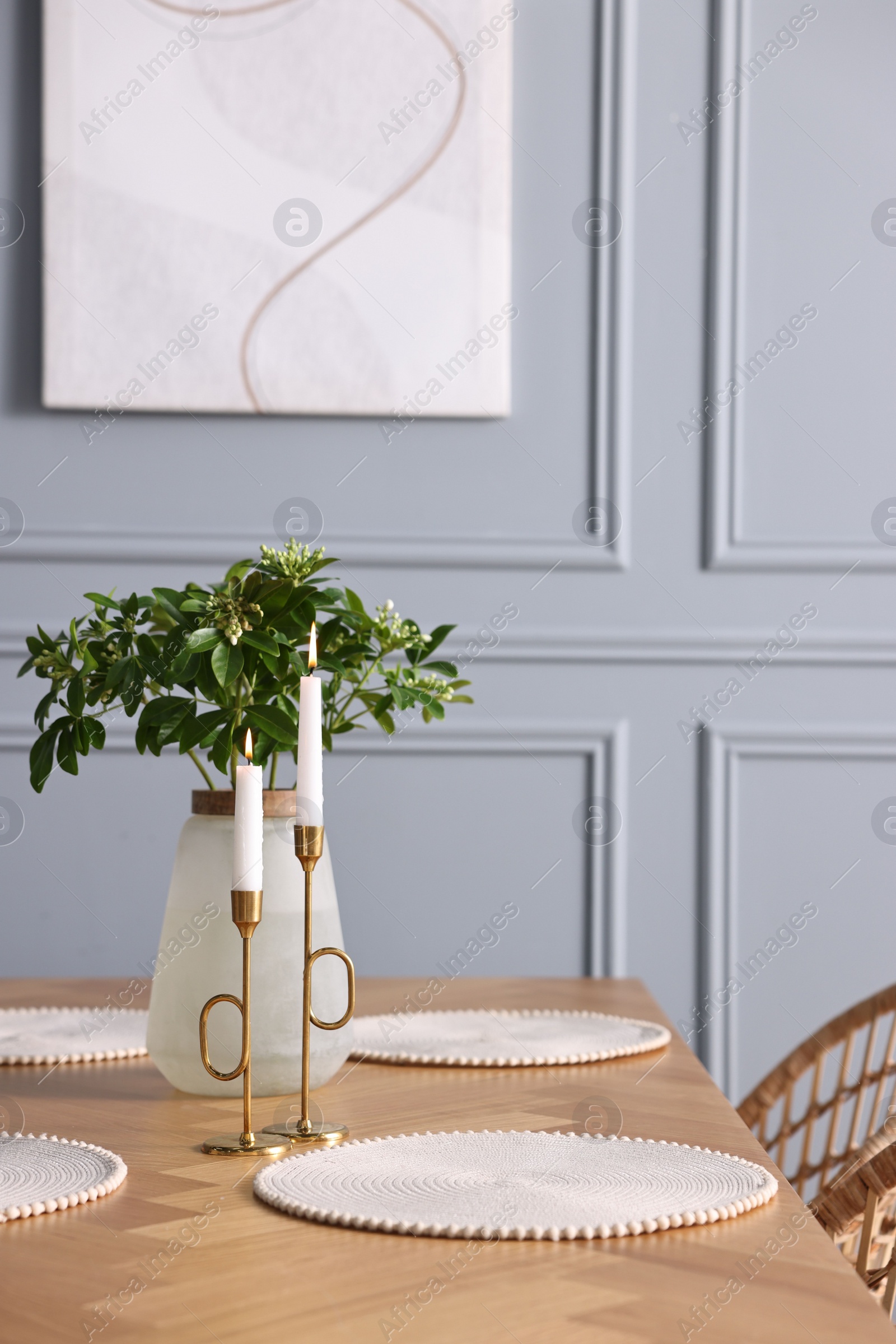 Photo of Vase with green branches and burning candles on wooden table in stylish dining room