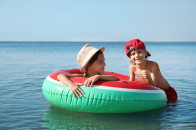 Cute little children with inflatable ring in sea on sunny day. Beach holiday
