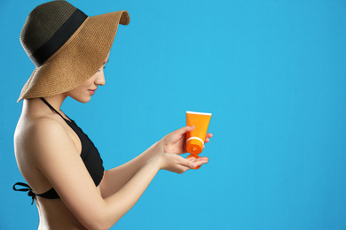 Young woman applying sun protection cream on blue background. Space for text