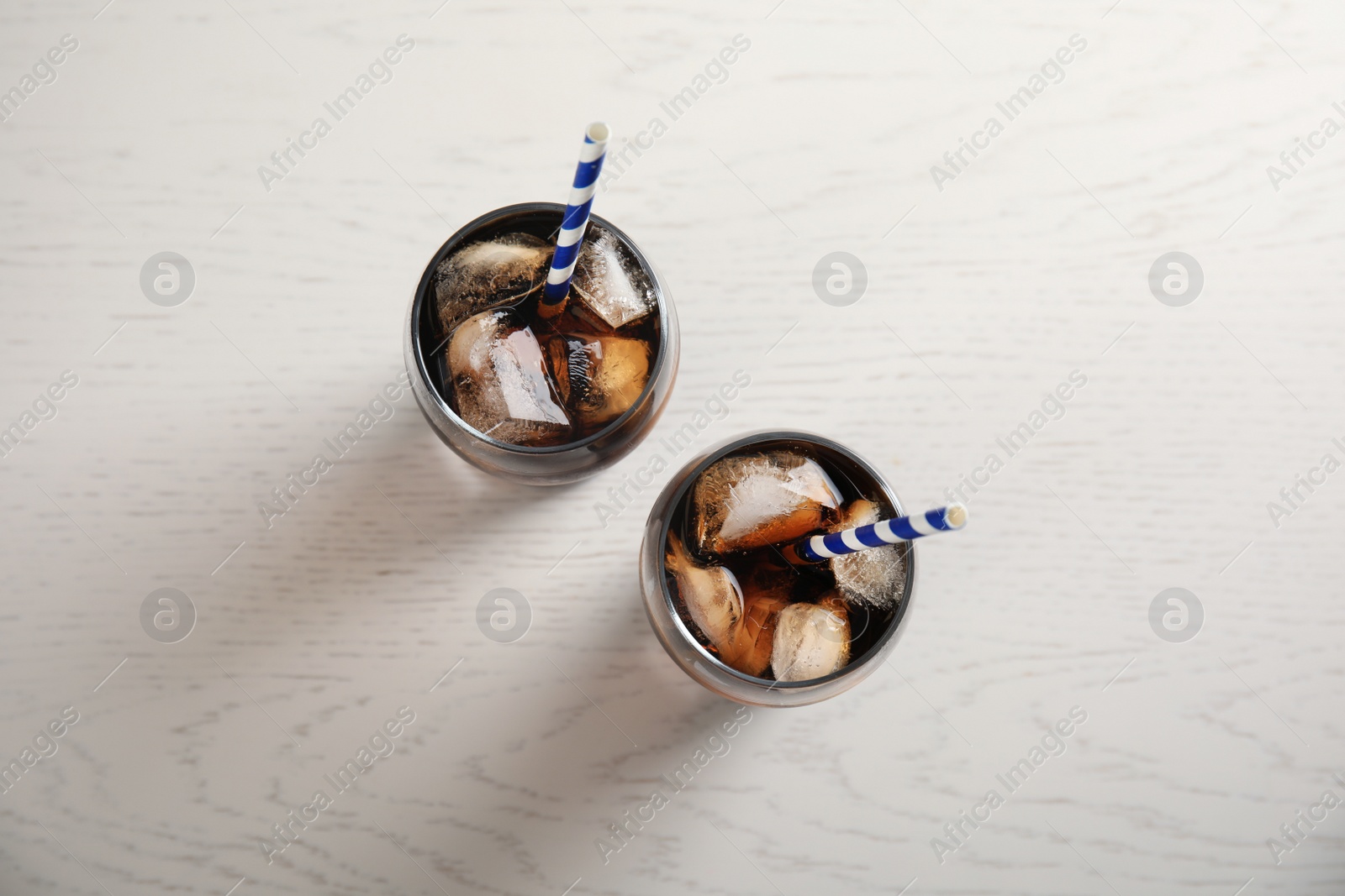 Photo of Glasses of refreshing cola with ice cubes and straws on white wooden background, top view