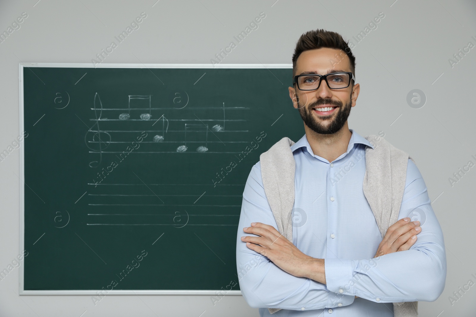 Photo of Teacher near green chalkboard with music notes in classroom