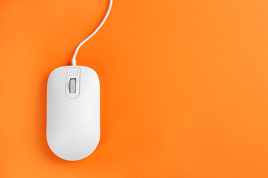 Photo of Modern wired optical mouse on orange background, top view. Space for text