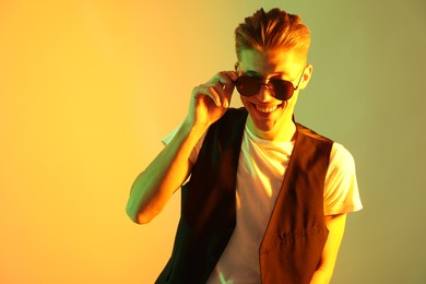 Photo of Stylish young man in sunglasses on color background in neon lights. Space for text