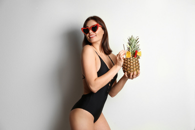 Photo of Beautiful woman in stylish swimsuit holding tropical cocktail on light grey background