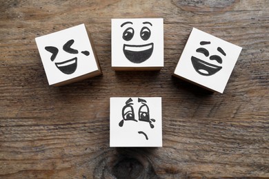 Photo of Cubes with sad and funny faces on wooden table, flat lay. Bullying concept