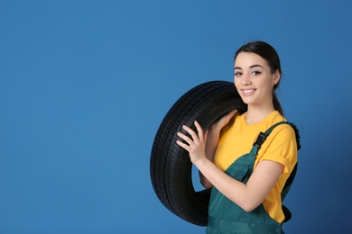 Photo of Female mechanic in uniform with car tire on color background