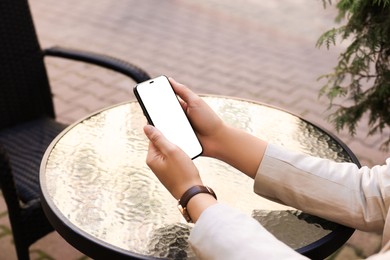 Photo of Woman using smartphone at table in cafe outdoors, closeup