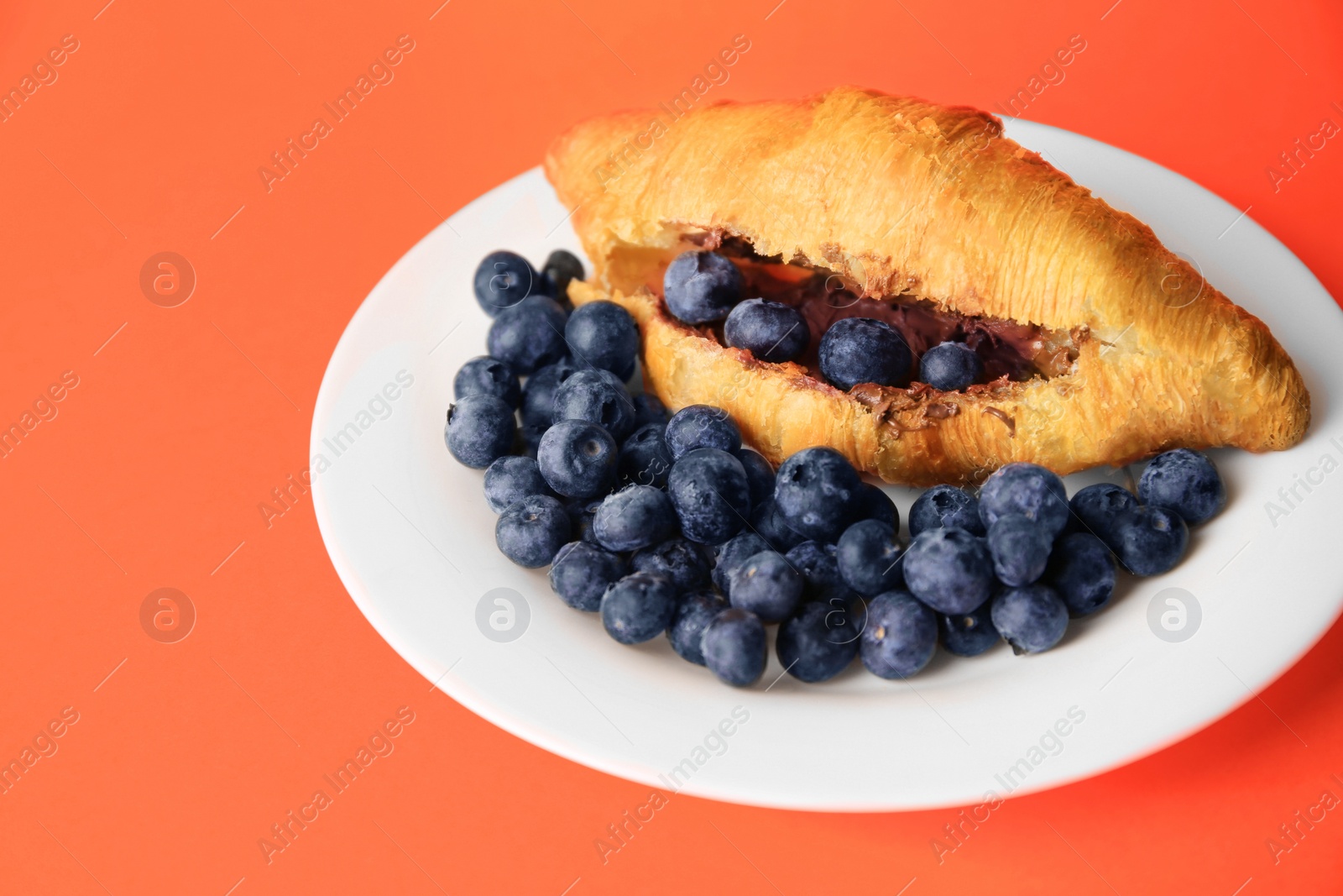 Photo of Tasty croissant with chocolate paste and blueberries on orange background, space for text