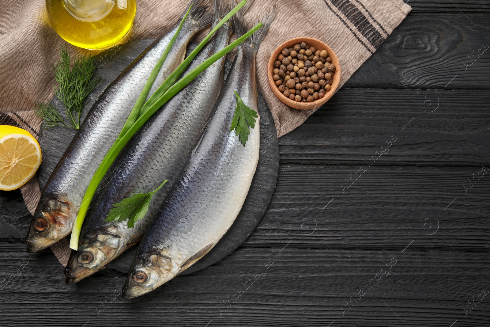 Photo of Delicious salted herrings and ingredients on black wooden table, flat lay. Space for text