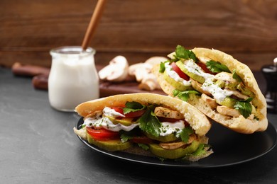Delicious pita sandwiches with grilled vegetables and sour cream sauce on black textured table. Space for text